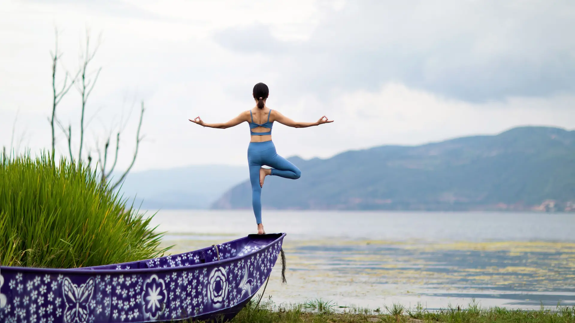 A woman balances in tree pose on a shore