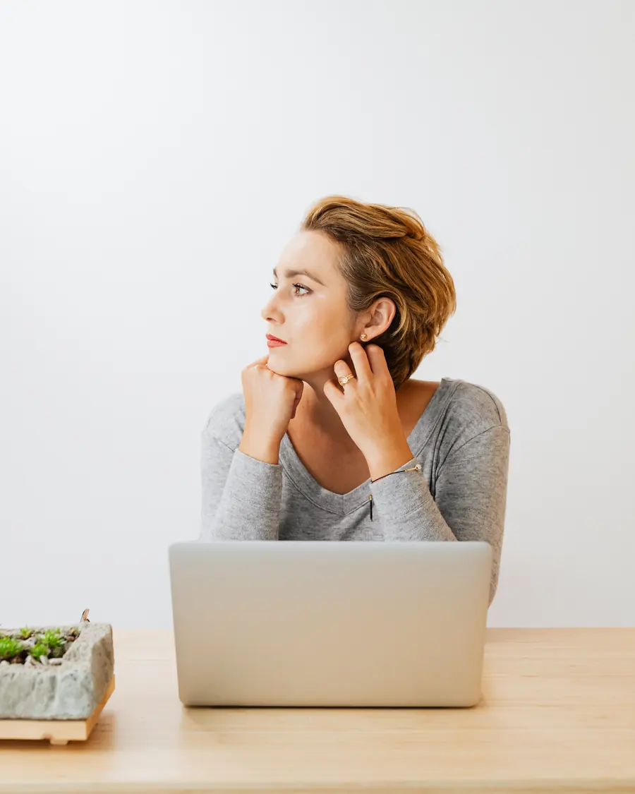 A woman at a laptop holds the back of her neck