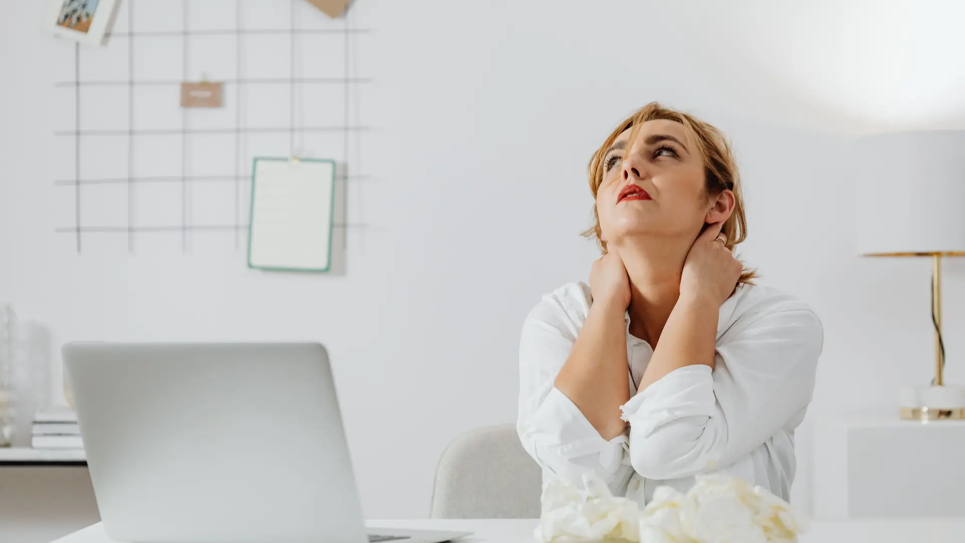 A woman at a desk holds her neck with both hands