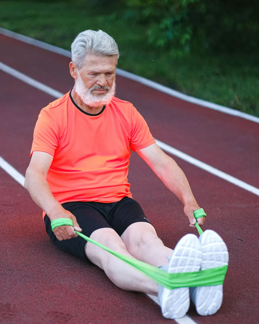An older man stretches a resistance band on a running track