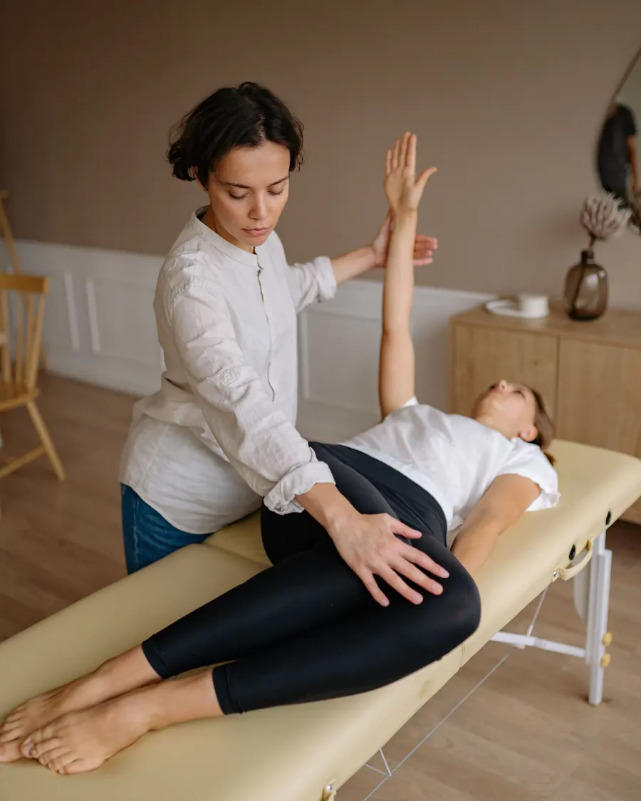 A physiotherapist raises the arm of a patient lying on a couch