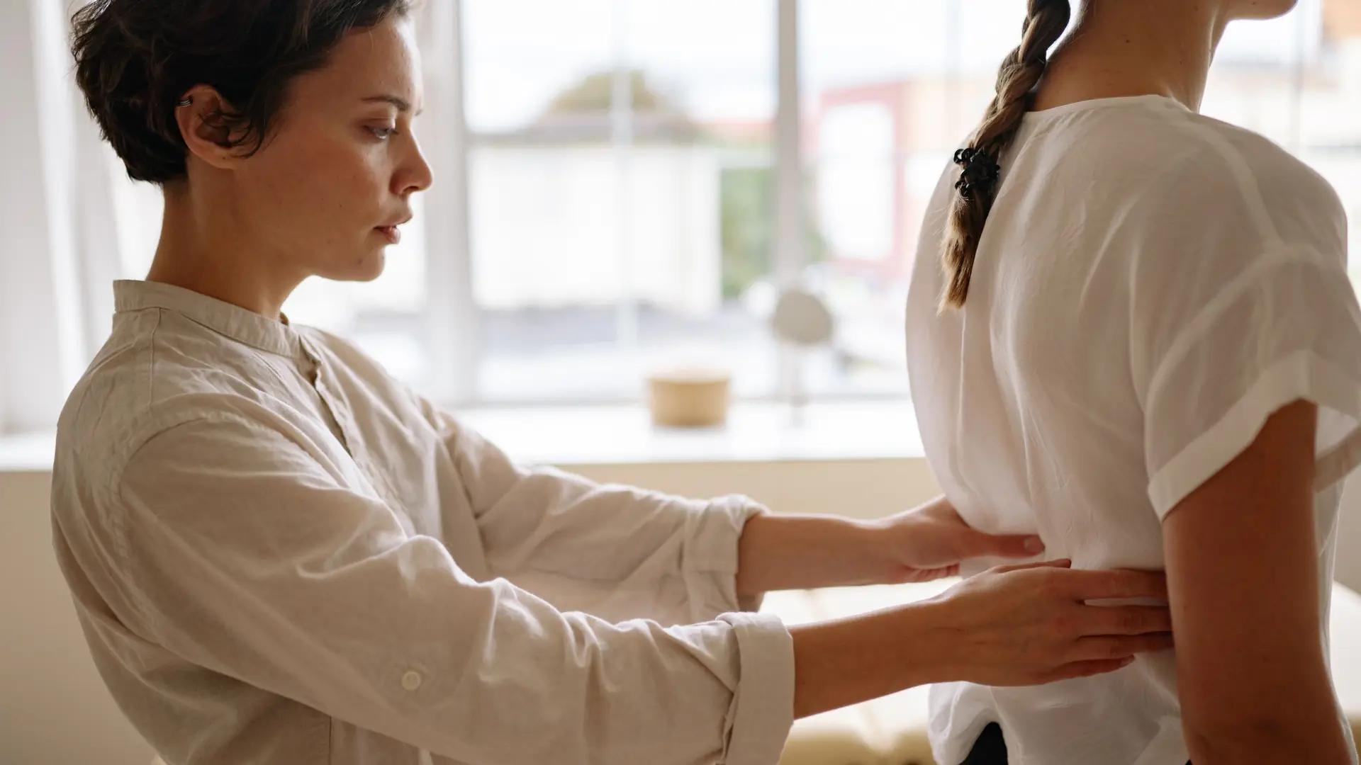 A physiotherapist’s hands on a patient’s back in window light
