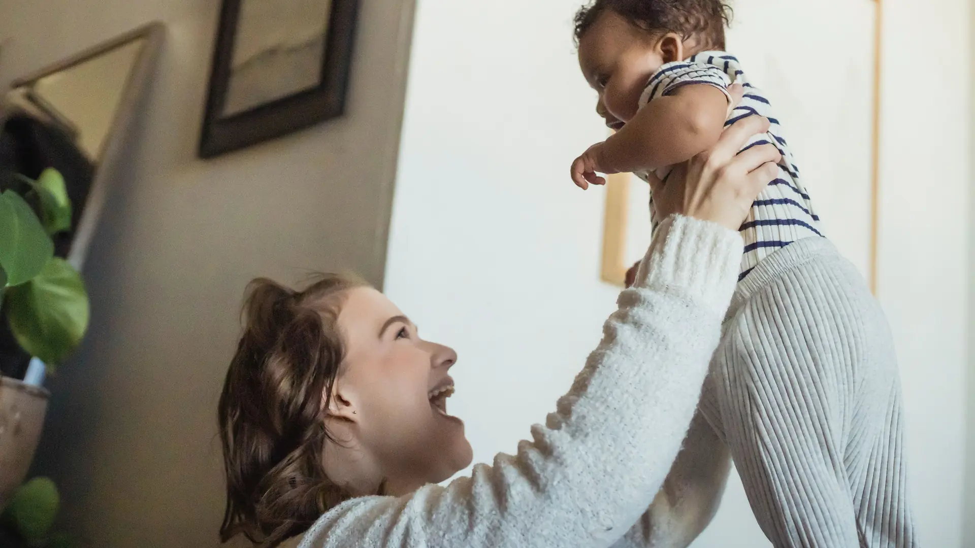 A mother lifts her baby into the air at home